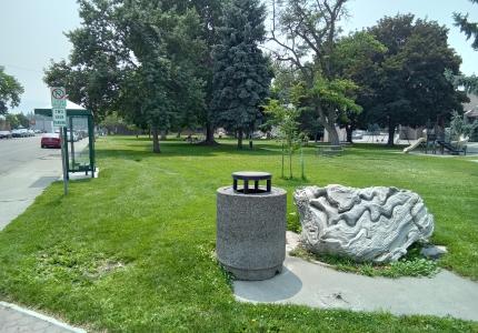 A park with a large white rock beautiful trees and a playground.