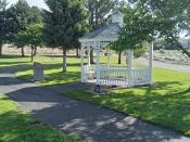 A white Gazebo on a walking path surrounded by trees in a park.