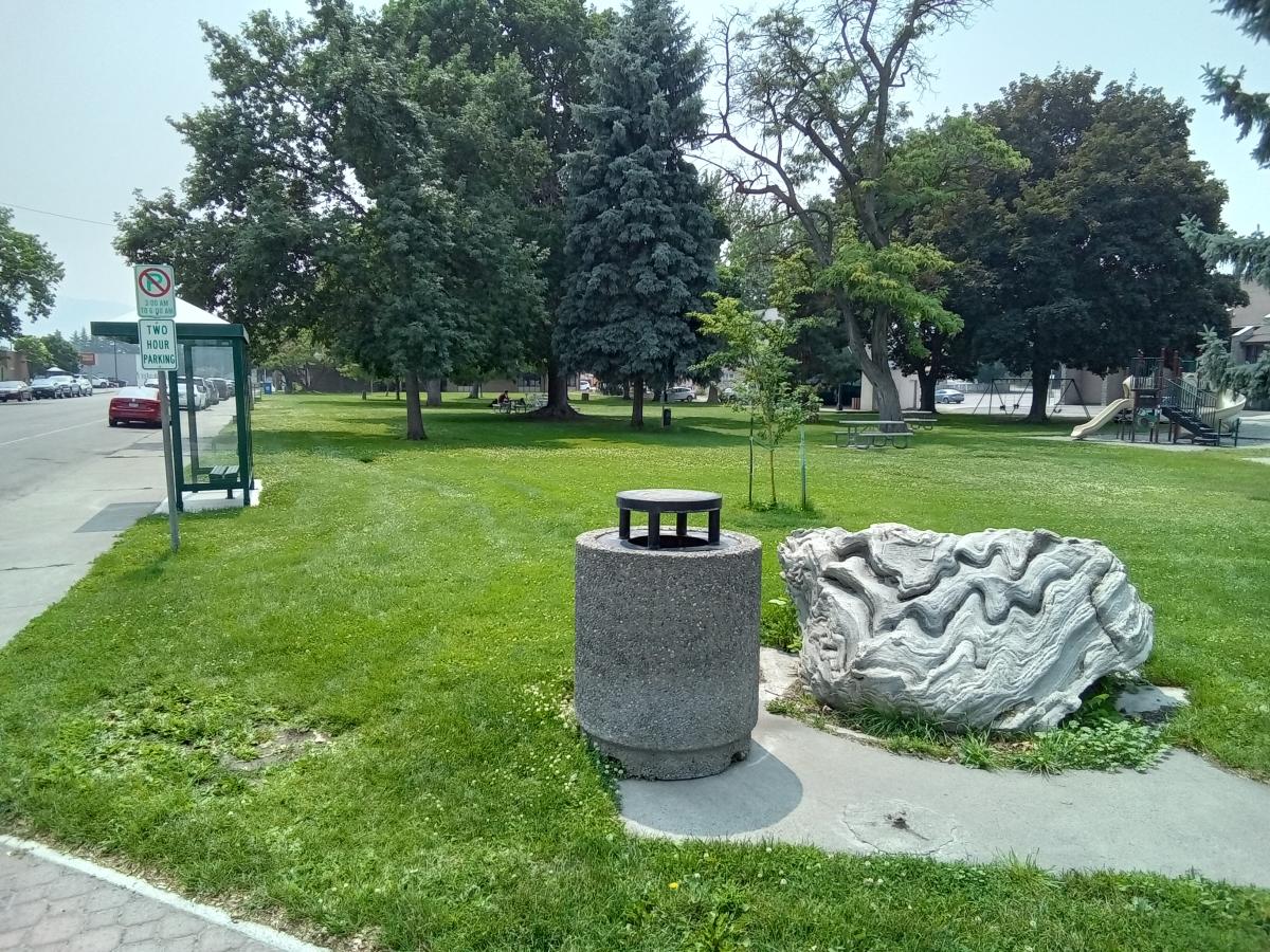 A park with a large white rock beautiful trees and a playground.